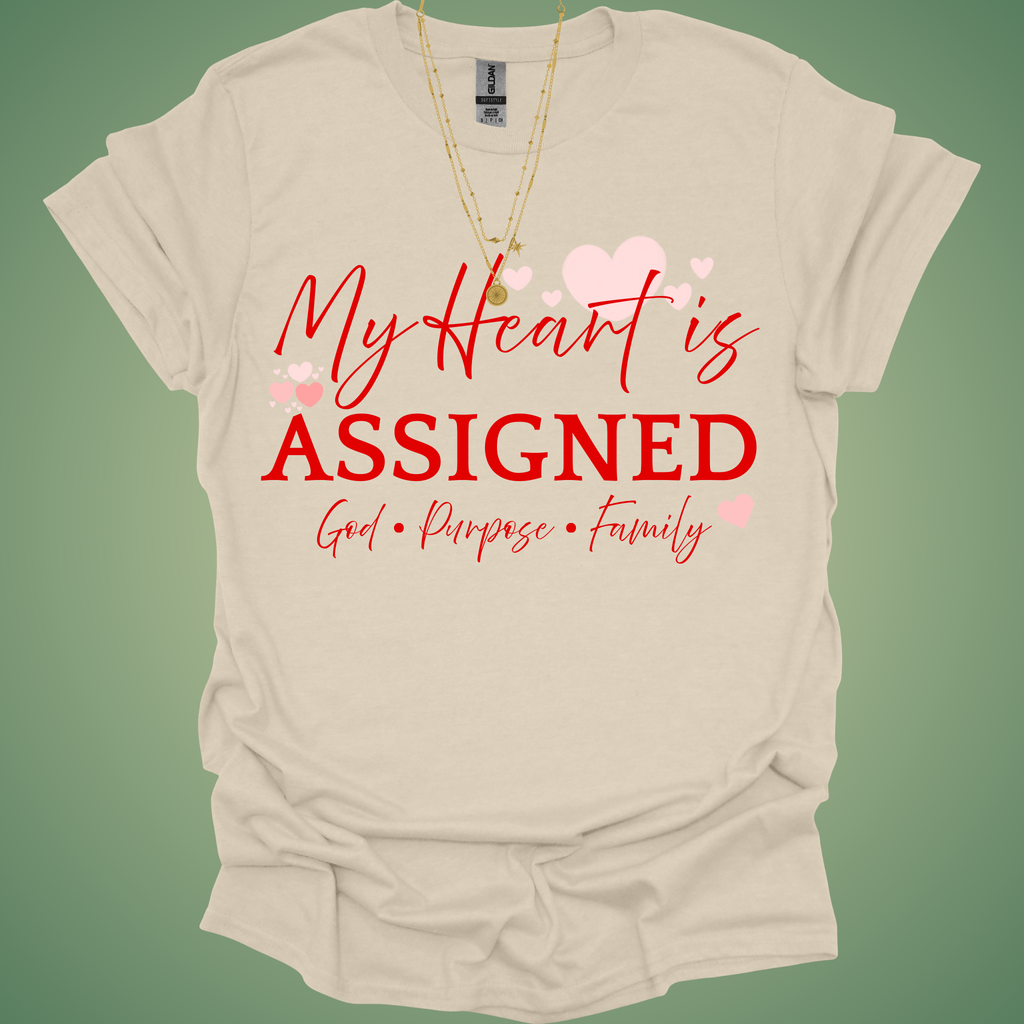 Beige t-shirt with red text 'My Heart is Assigned' on a green background